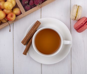 top view cup of tea with macaroons and cinnamon on a white background
